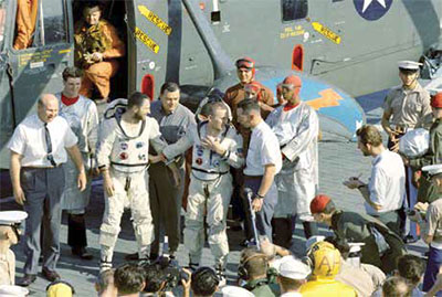 После спуска экипажа «Джемини-7» с орбиты. В центре (слева направо): астронавты Ловелл и Борман разговаривают с доктором Майнерсом у спасательного вертолета на борту авианосца Wasp. 18 декабря 1965 года. Фотография НАСА2